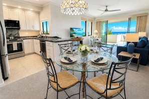 Una cocina moderna con armarios blancos, un comedor con mesa de vidrio y vista al océano.