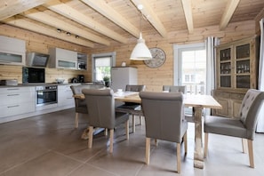A modern kitchen with wooden beams, a dining area with a table and chairs, and a clock on the wall. - Mountain Forest Lodge Time Out (Schierke)