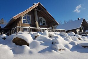 Eine Holzhütte mit einem steilen Dach, großen Fenstern und einer verschneiten Veranda.