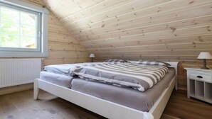 Un dormitorio con techo inclinado, una cama con ropa de cama a rayas, una mesita de noche y una ventana.