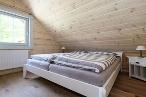Ein Schlafzimmer mit schrägen Wänden, einem Bett mit gestreifter Bettwäsche, einem Nachttisch und einem Fenster.