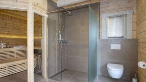 Un baño moderno con cabina de ducha de vidrio, inodoro y ventana con persianas.