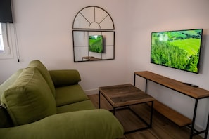A living room with a green sofa, a wooden coffee table, a TV mounted on the wall, and a mirror above the coffee table. - Deluxe Apartment No. 1 – Charm and Comfort in El Puerto de Santa María (El Puerto de Santa María)
