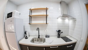 A compact kitchen with a built-in refrigerator, a sink, and a microwave. - Deluxe Apartment No.1 – Charm and Comfort in El Puerto de Santa María (El Puerto de Santa María)