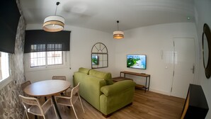 A modern living room with a green sofa, a dining table with chairs, a TV mounted on the wall, and a wooden floor. - Deluxe Apartment No.1 – Charm and Comfort in El Puerto de Santa María (El Puerto de Santa María)