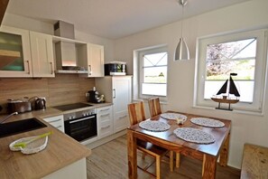 A modern kitchen with white cabinets, a wooden dining table with placemats, and a view of the outdoors through windows. - favorite spot by the sea (Norden-Norddeich)