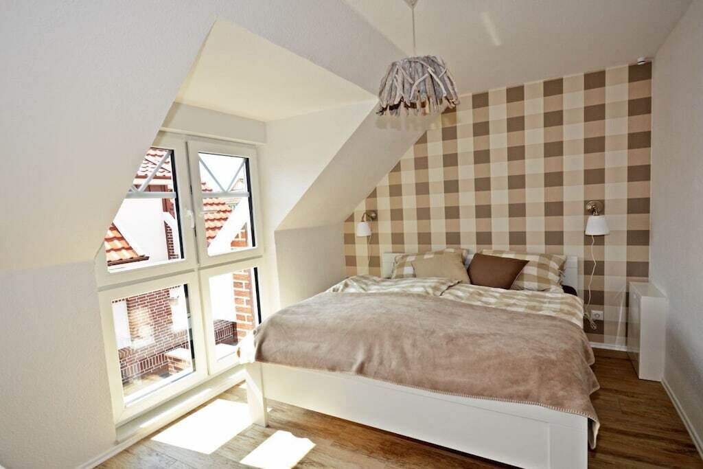 A bedroom with a sloped ceiling, a bed with a beige blanket, two bedside lamps, and a checkered wall pattern.