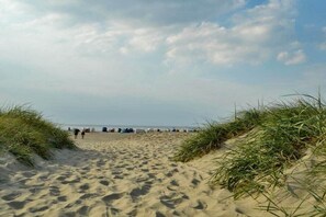 Ein Sandweg am Strand, begrenzt von Dünen, der zum Meer führt.