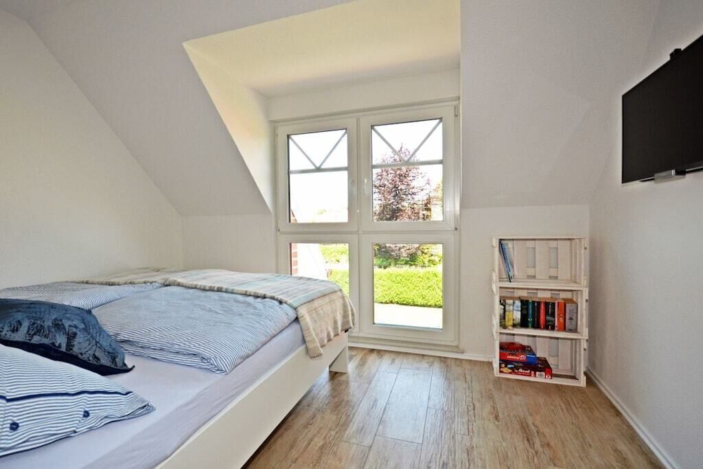 Un dormitorio con techo inclinado, una cama, un ventanal y una estantería.