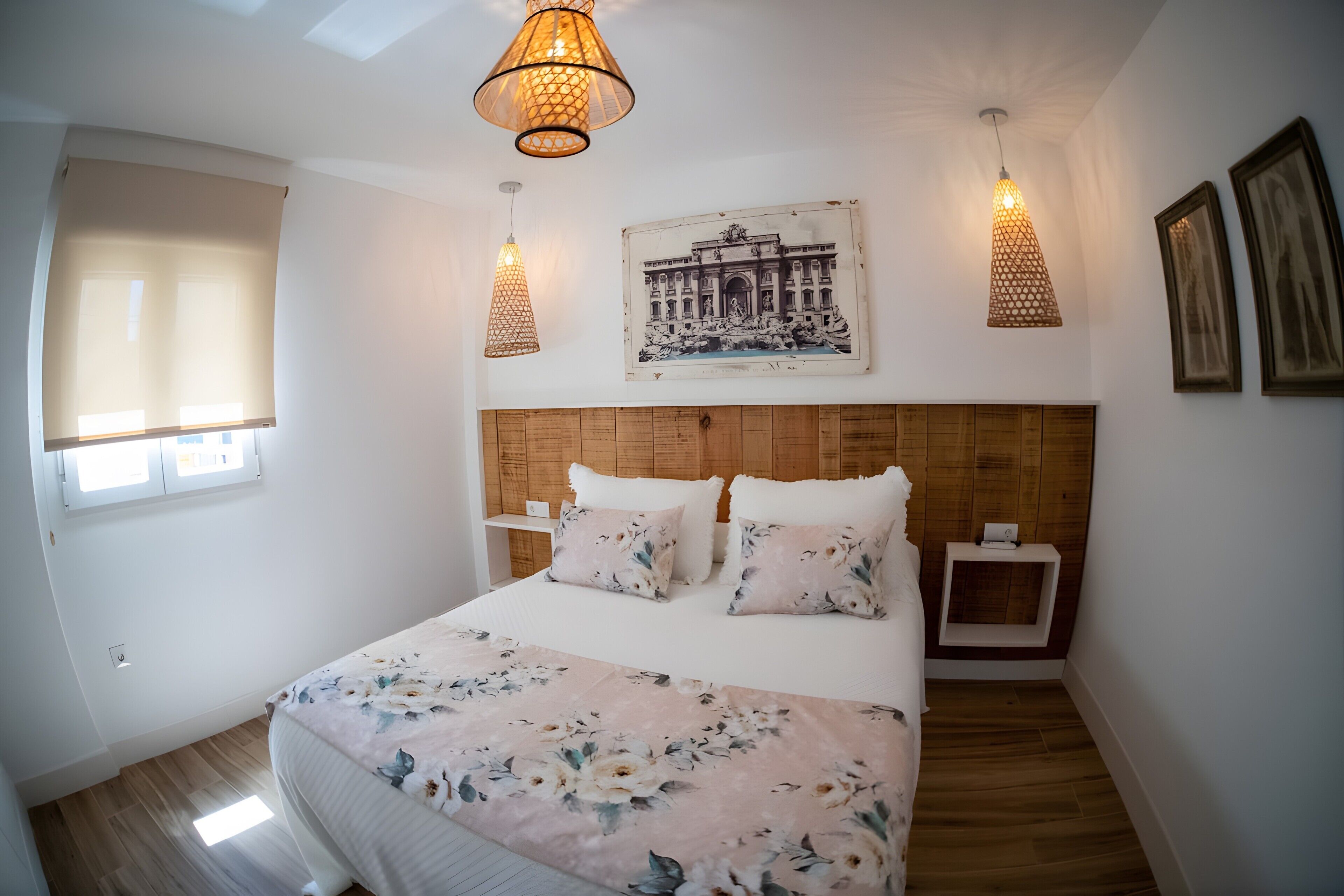 Ein Schlafzimmer mit einem hölzernen Kopfteil, einer blumigen Tagesdecke, zwei Nachttischen und einem an der Wand hängenden Bild.