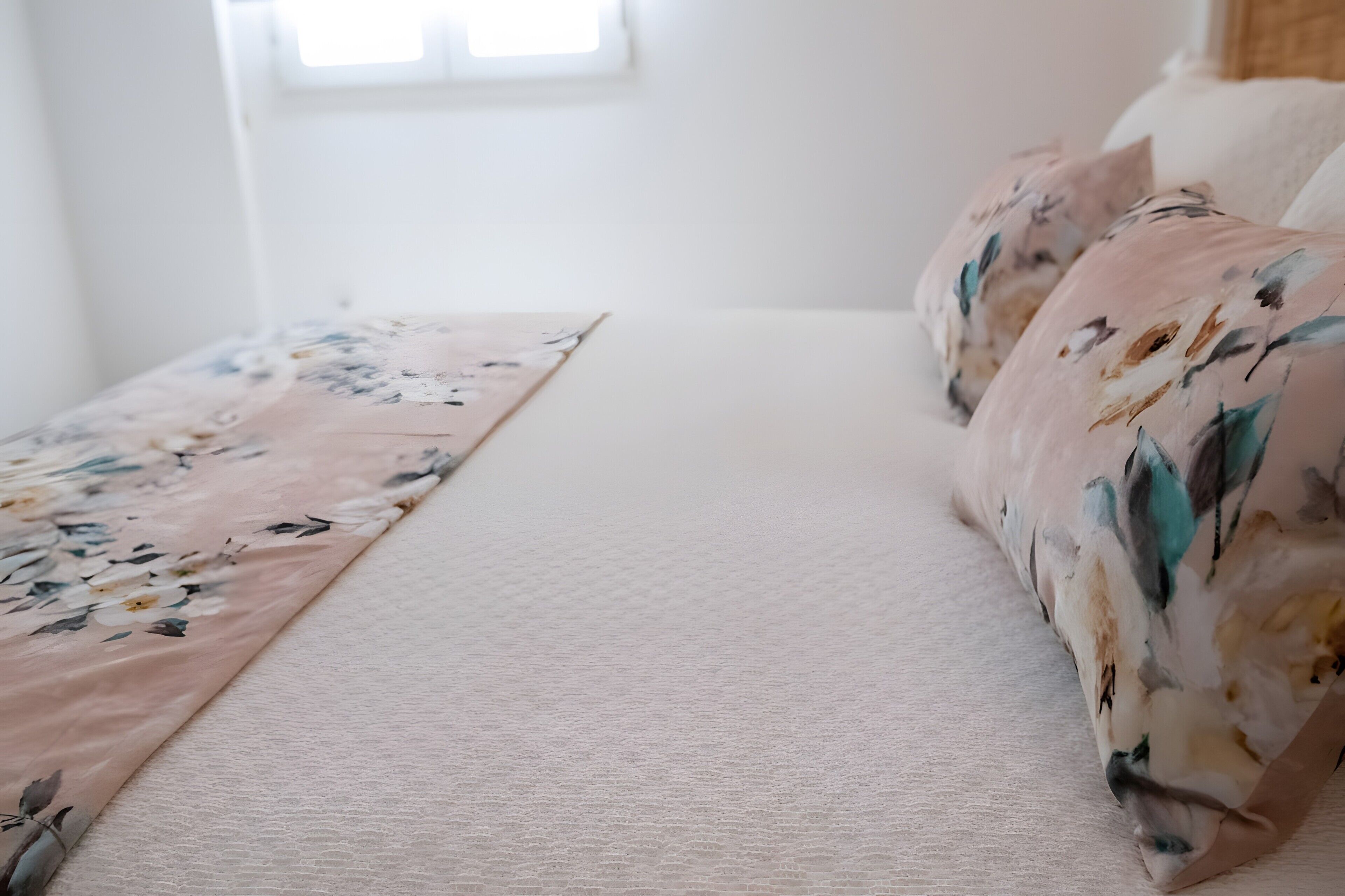 A bed with a floral bedspread and a plain pillow.