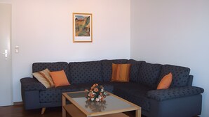 Ett vardagsrum med en hörnsoffa, ett soffbord och en inramad tavla på väggen.
