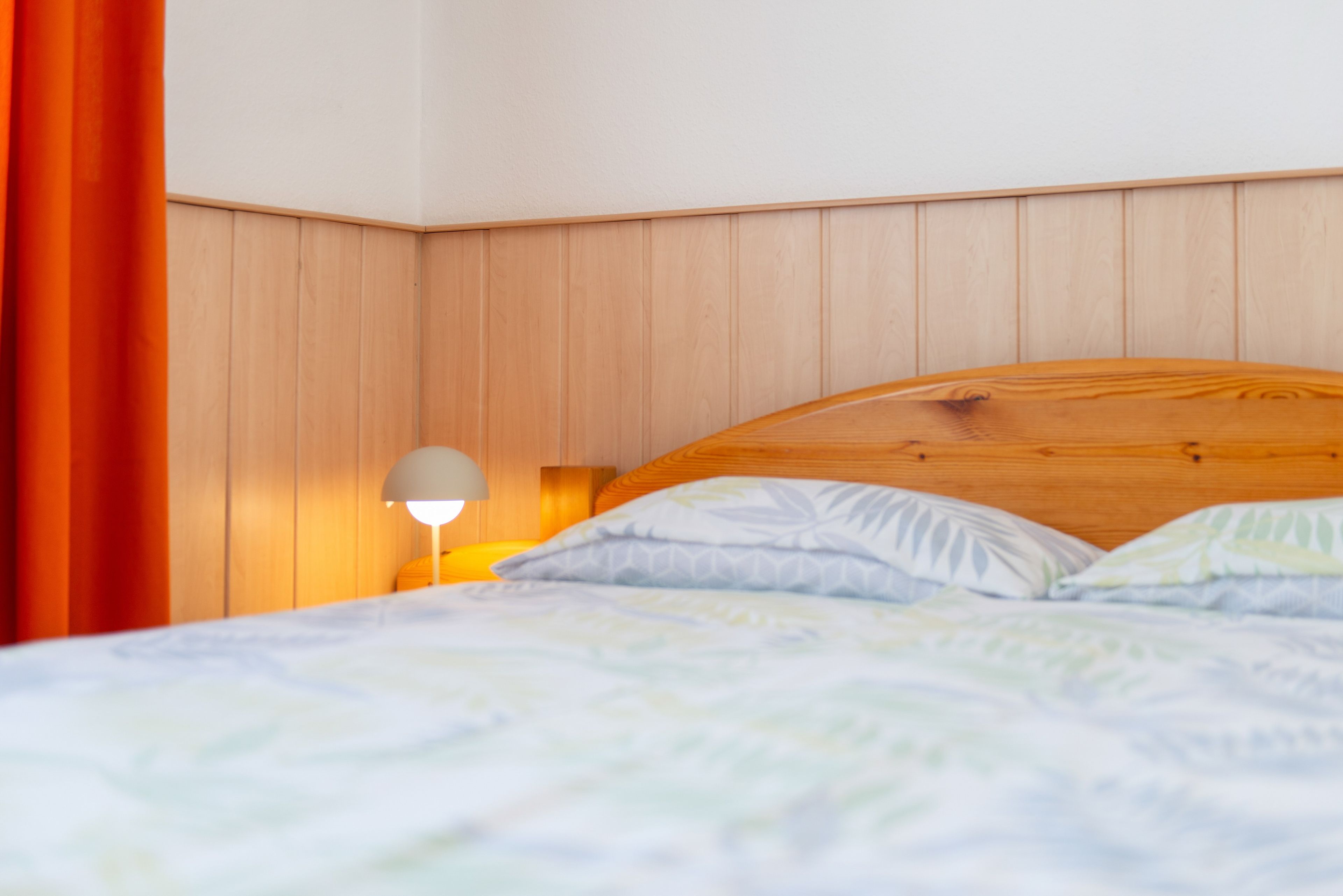 Ein Bett mit Holz-Kopfstück, einer Nachttischlampe und einer gemusterten Bettdecke.