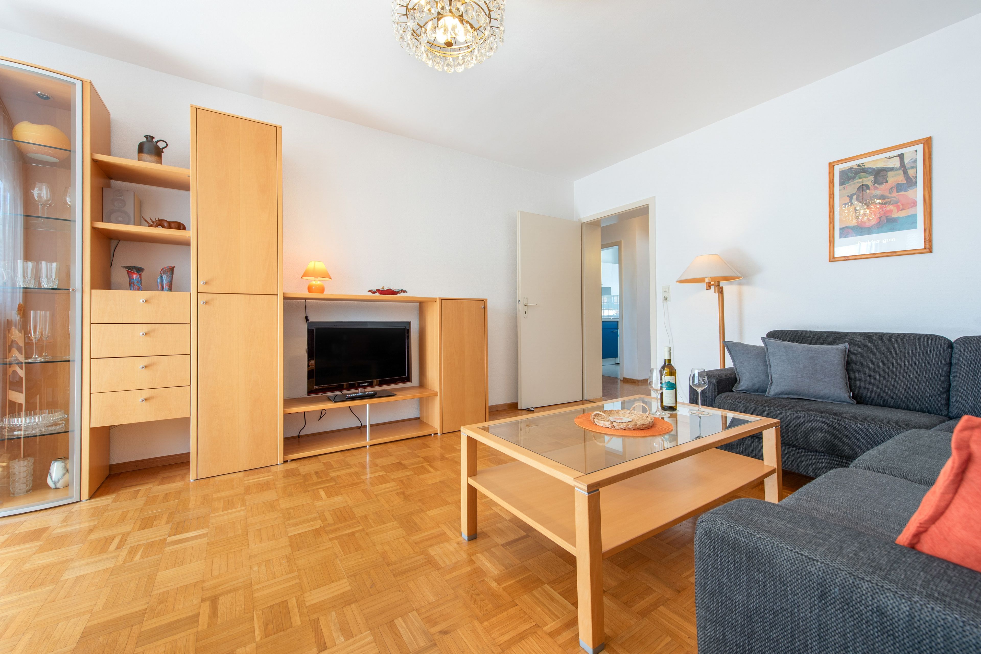 Een moderne woonkamer met een flatscreen televisie, houten meubels en een glazen salontafel.