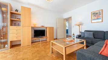 Een moderne woonkamer met een flatscreen televisie, houten meubels en een glazen salontafel.