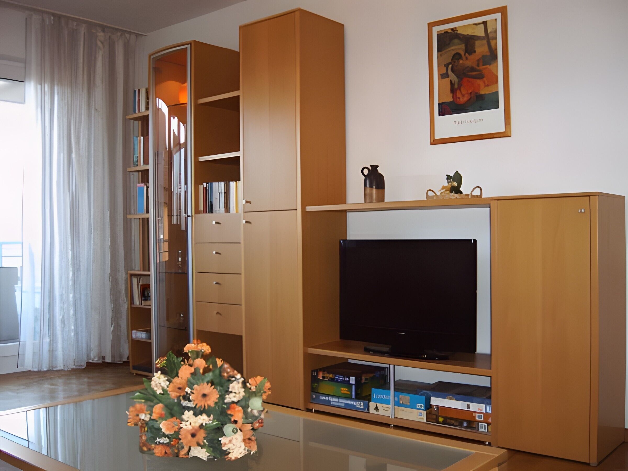Un salon avec un téléviseur à écran plat, une bibliothèque, une table basse agrémentée d’un arrangement floral et un tableau accroché au mur.