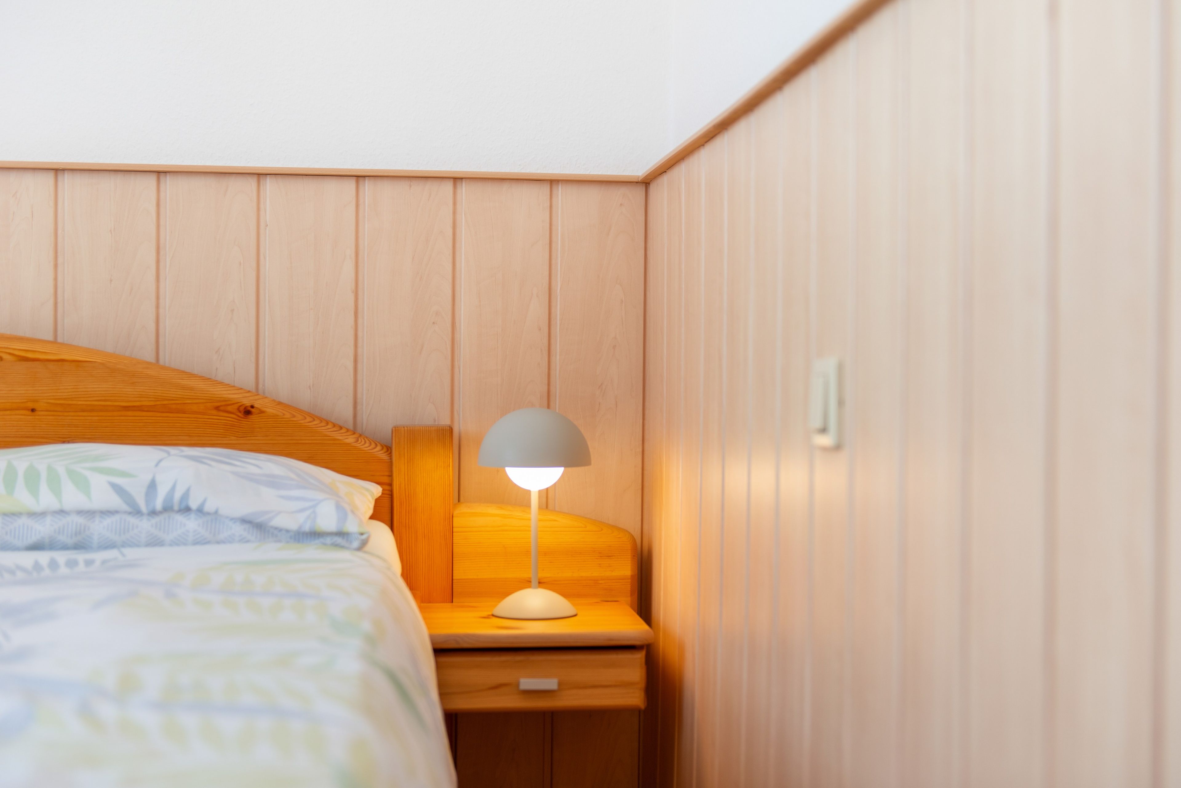 Een slaapkamer met een houten hoofdbord, een nachtkastje met een lamp en een bed met beddengoed met een patroon.