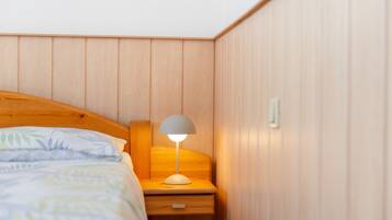 Een slaapkamer met een houten hoofdbord, een nachtkastje met een lamp en een bed met beddengoed met een patroon.
