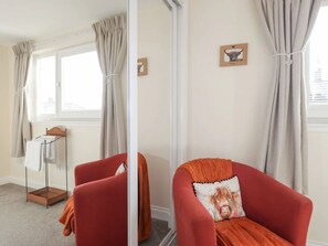 Ein Zimmer mit einem roten Sessel, einem kleinen Tisch mit einem Handtuch und einem Fenster mit Vorhängen.