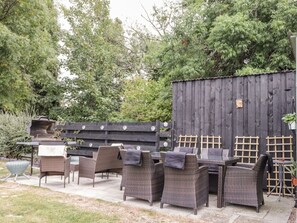 Een terras buiten met rieten meubels en een barbecue.