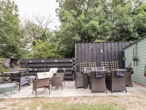 Eine Terrasse im Freien mit Korbmöbeln, einem Grill und einem Holzzaun.