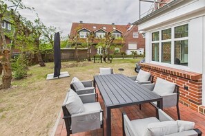 A patio with a table and chairs, a brick wall, and a view of a residential area. - Holiday apartment Norderloog 3 (Langeoog)