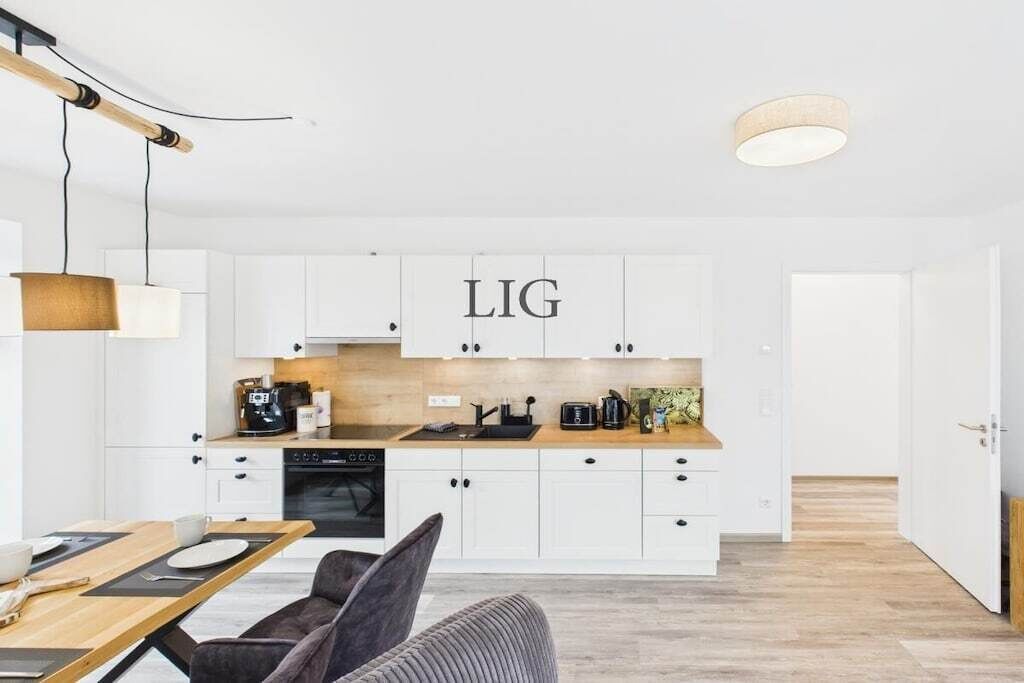 A modern kitchen with white cabinetry, a wooden countertop, and a dining area with a table and chairs.