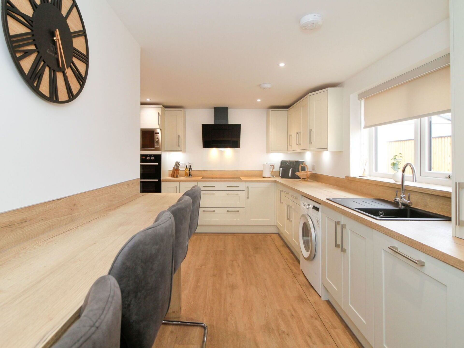 A modern kitchen with white cabinetry, a wooden countertop, a built-in washing machine, and a large wall clock.