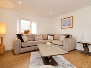 Een moderne woonkamer met een beige bank, een glazen salontafel en een houten vloer.