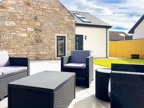 Een terras met rieten meubilair, een stenen muur en een klein gebouw met een deur en raam.
