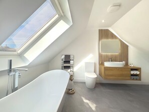 Ein modernes Badezimmer mit Dachfenster, einer freistehenden Badewanne, einer Toilette und einem Waschtisch mit Spiegel.