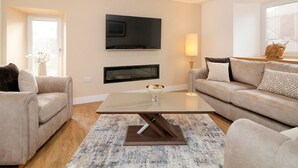 Uma sala de estar moderna com uma televisão de tela plana, dois sofás, uma mesa de centro e um tapete estampado.
