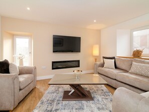 Ein modernes Wohnzimmer mit einem Flachbildfernseher, zwei Sofas, einem Couchtisch und einem gemusterten Teppich.