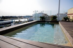 Une piscine sur le toit, avec une eau cristalline, entourée d’une terrasse en bois et de plantes en pot.