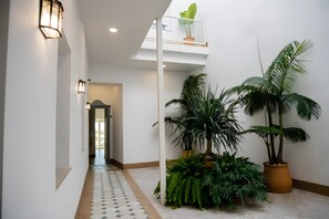 Un pasillo con suelo de baldosas, plantas en macetas e iluminación empotrada en la pared.