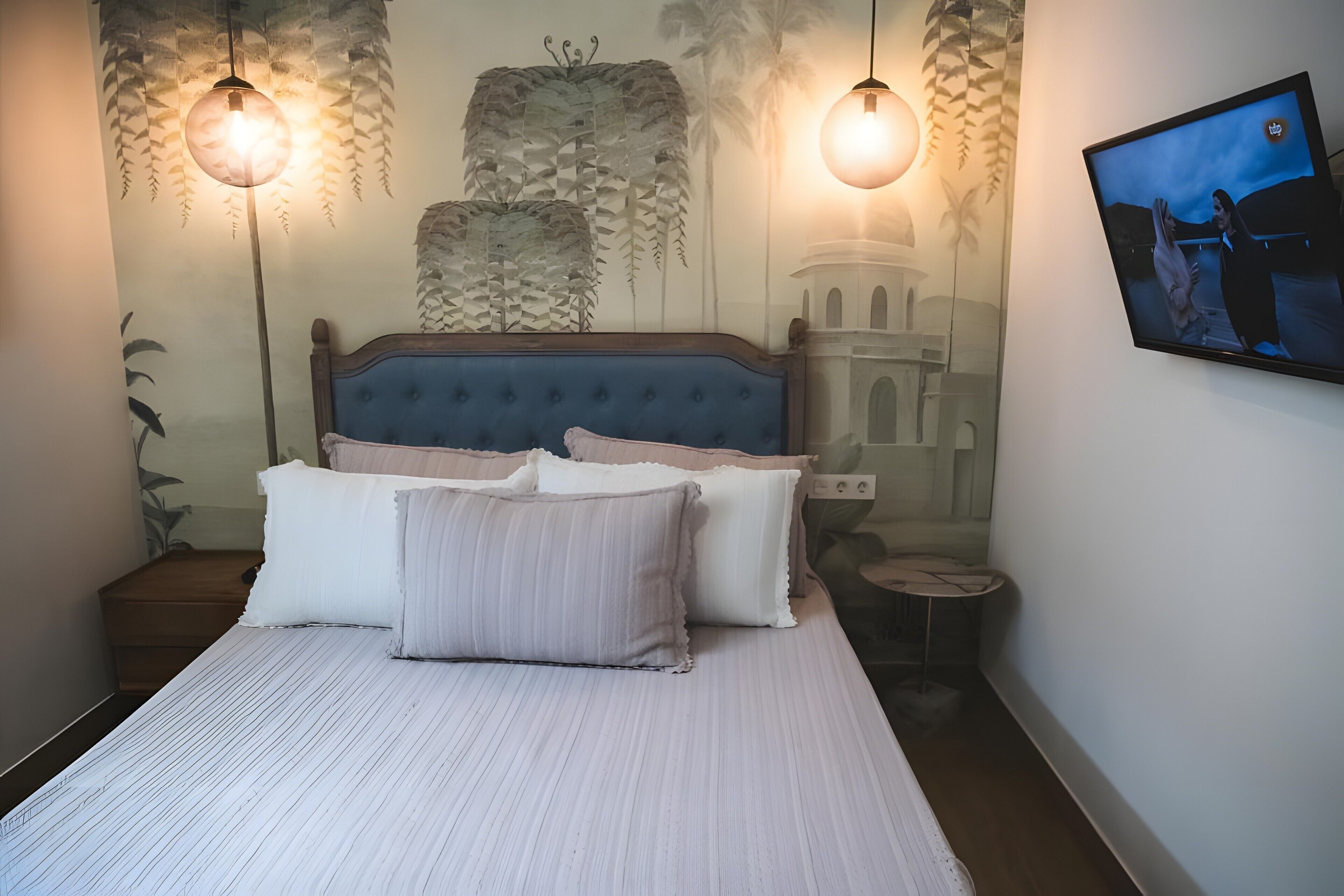 Une chambre à coucher avec un lit, des oreillers, un téléviseur fixé au mur et des luminaires suspendus.