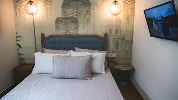 Une chambre à coucher avec un lit, des oreillers, un téléviseur fixé au mur et des luminaires suspendus.