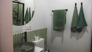 Kylpyhuoneessa on pyöreä peili, pesuallas, wc-istuin ja pyyhkeet, jotka on ripustettu pyyhetelineeseen.