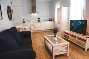 Ein modernes Wohnzimmer mit einem dunklen Sofa, einem Glastisch und einem Fernseher auf einem Holzgestell.