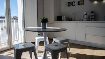 Une cuisine moderne avec une table ronde, deux tabourets, une plante en pot et un coin cuisine.