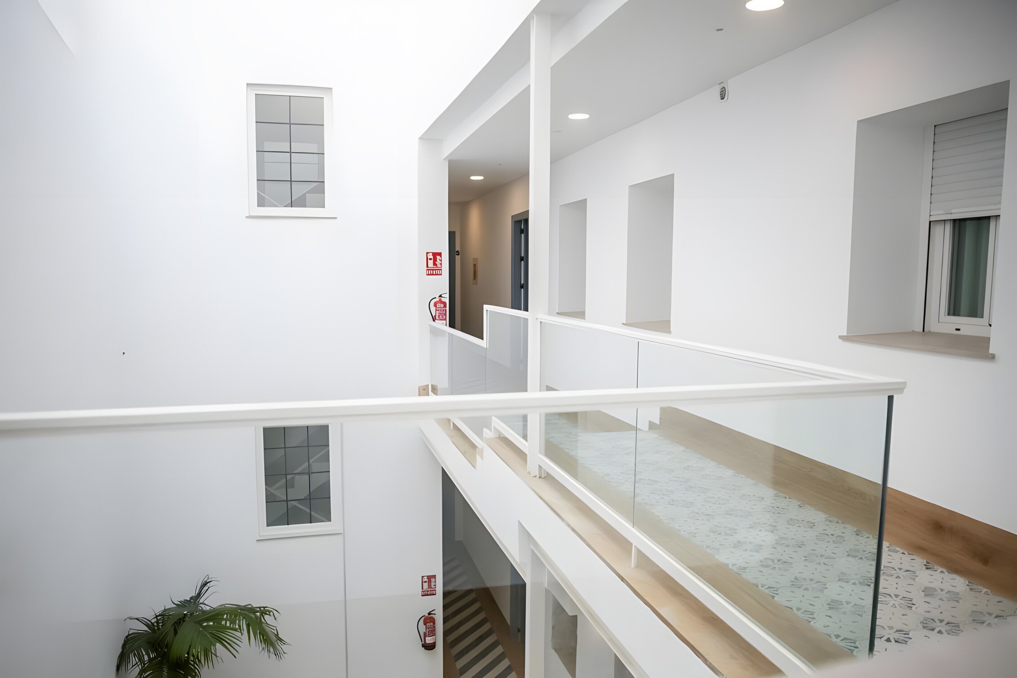 Een meerlaags interieur met een glazen balustrade, een brandblusser en een potplant.