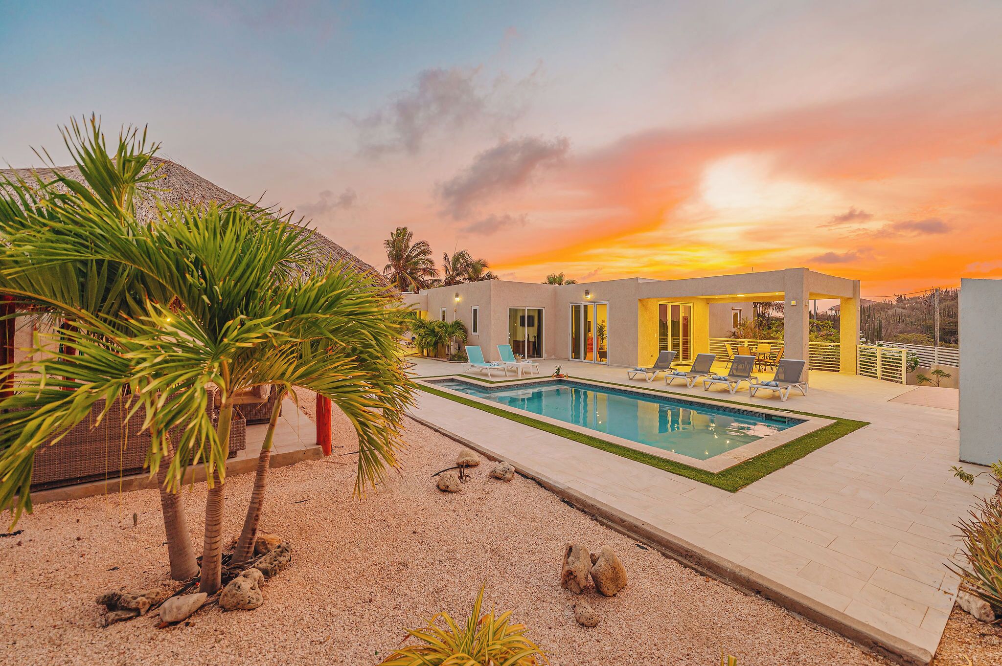 A modern pool area with a clear pool, lounge chairs, and a sunset view.