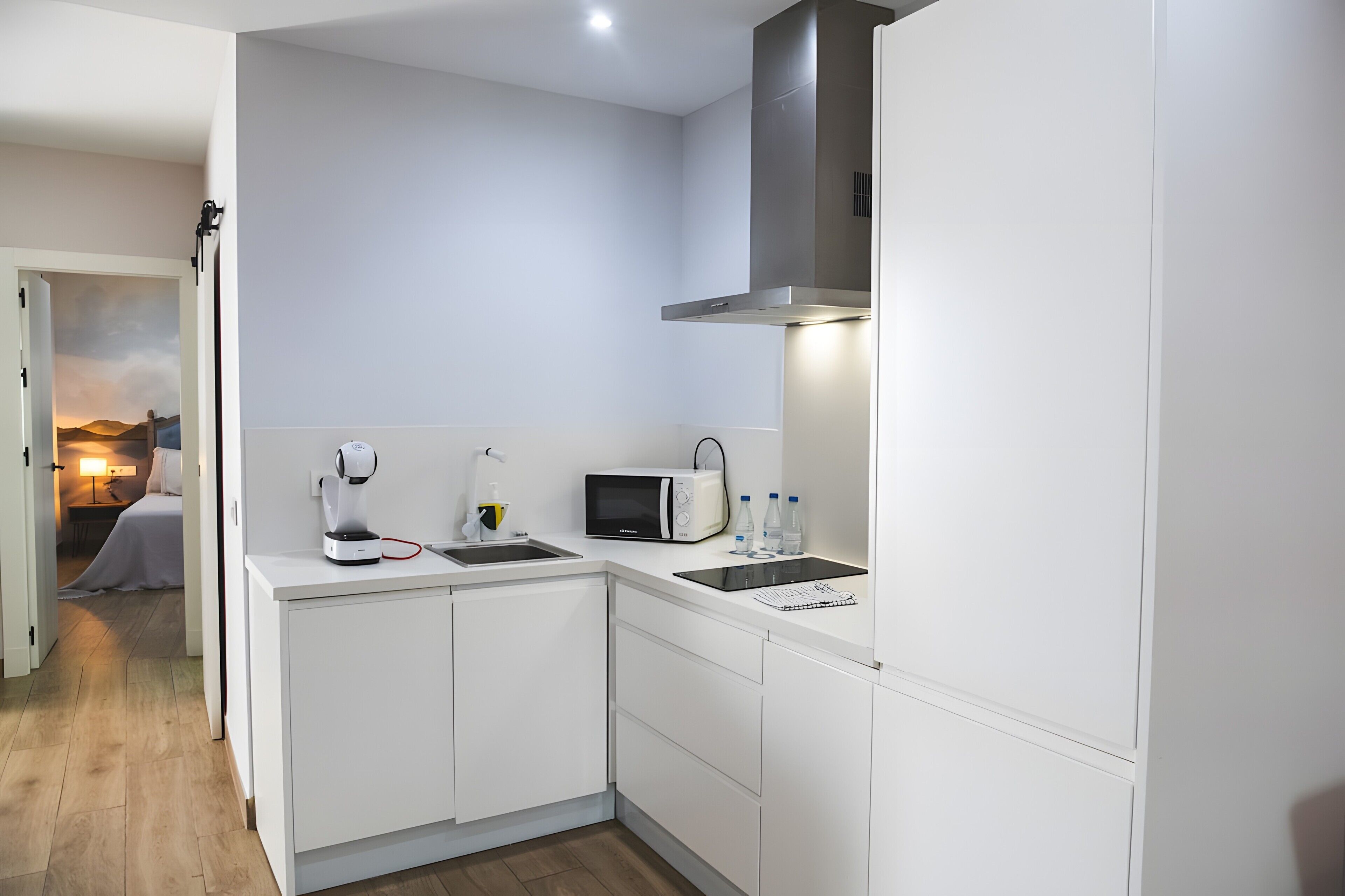 Een moderne keuken met witte kastjes, een magnetron, een waterkoker en een spoelbak.