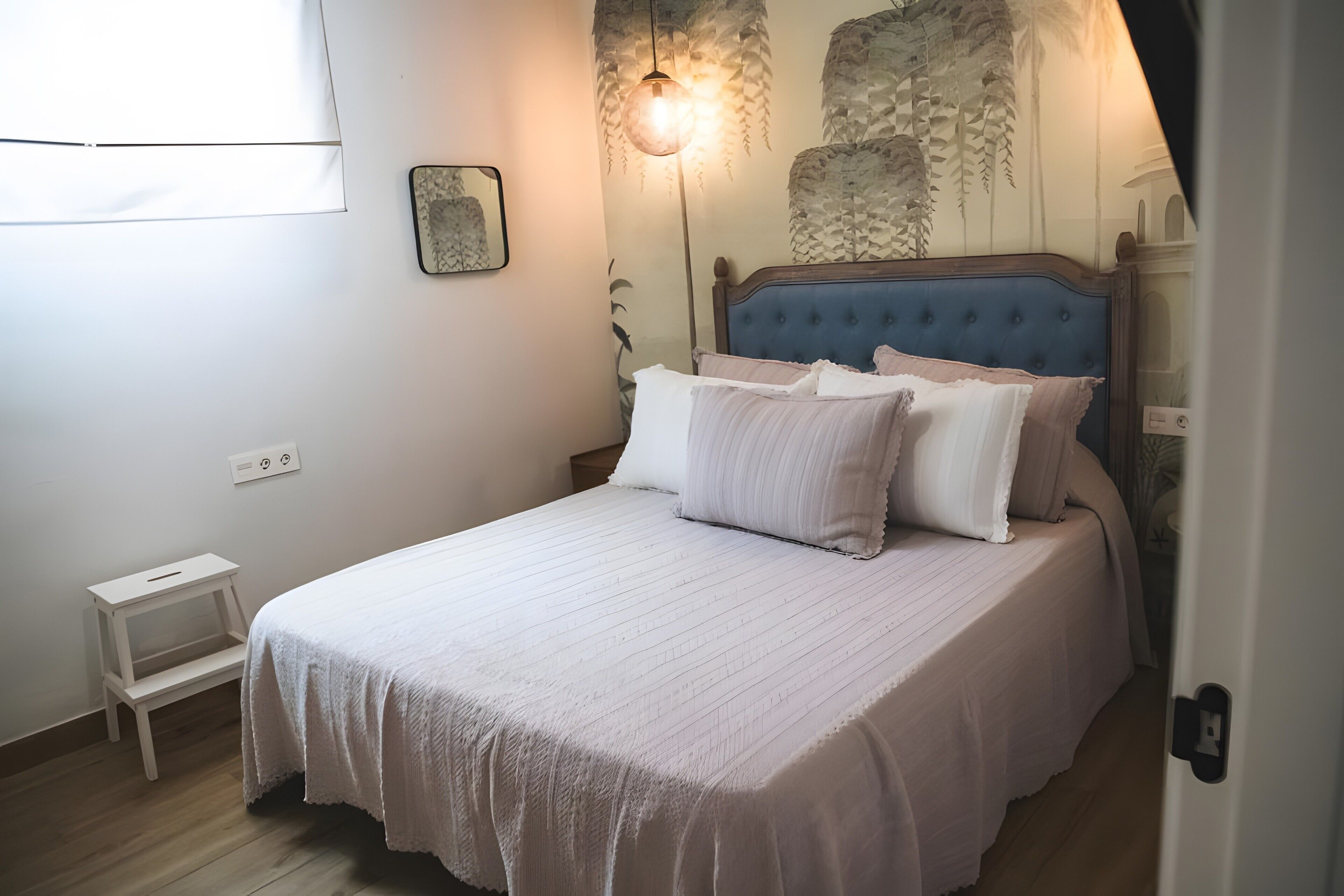 A bedroom with a bed, bedside table, and a wall-mounted lamp.