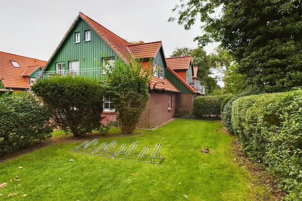 A green house with a red roof, a well-maintained lawn, and a metal bike rack.
