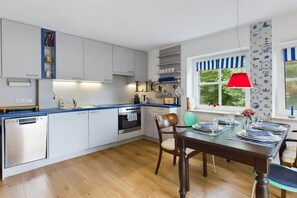 Une cuisine moderne avec des armoires blanches, un four encastré et un coin repas avec une table dressée pour quatre personnes.
