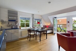 Une cuisine moderne avec une table à manger pour quatre personnes, une chaise rouge et un canapé rouge dans une pièce lumineuse donnant sur l’extérieur.