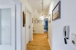 A hallway with a wooden floor, white walls, and a mounted telephone. - Holiday apartment Island Love (Langeoog)