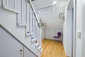 A modern interior with a staircase, a purple chair, and a white wall with a logo. - Holiday apartment Island Love (Langeoog)