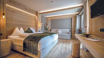 A modern bedroom with a large bed, a sofa, a wooden floor, and a flat-screen TV.